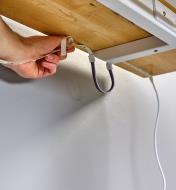 Personne installant un luminaire-ruban sous le plateau d'une table et contournant un tréteau à l'aide d'un câble connecteur
