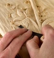 A carver uses a Flexcut #6 palm gouge on a floral relief carving