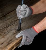 Wearing a pair of lightweight work gloves while prying a nail from a board