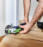 Using an OSC 18 oscillating tool equipped with the saw blade to trim wooden flooring flush to a wall