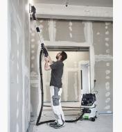 A worker sands the very top of a wall with the Planex LHS 2 225