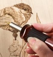 Personne dessinant un oiseau en pyrogravure sur bois à l’aide d’un fer à pyrograver multifonction