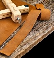 A band of leather shown next to the leather sheet it was cut from and a leather strap cutter