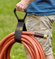 A gardener carries a coiled garden hose held in a tidy bundle with the easy-carry storage wrap