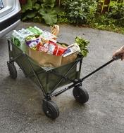 A folding cart being used to bring a load of groceries into a house after unloading them from a car
