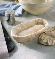 Housse à côté d'un banneton ovale doublé contenant de la pâte à pain