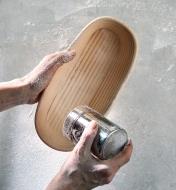 Using a stainless-steel flour shaker to dust the oval banneton with flour