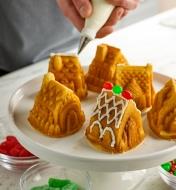 Personne décorant un des six petits gâteaux en forme de maisonnette posés sur une assiette