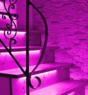 Escalier illuminé par un éclairage d'ambiance rose provenant de luminaires-rubans sous le nez des marches