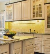 A kitchen counter and cabinets, with a light shining onto the counter from the upper cupboards