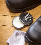 Paire de chaussures en cuir dont l'une a été enduite de cire pour le cuir Walrus Oil près d'une boîte de cire et d'un chiffon