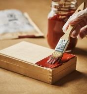 Brushing red milk paint onto the top of a small wooden box