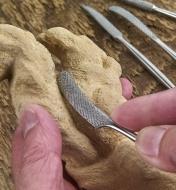 A woodworker uses a stainless-steel riffler to shape the pronounced contours of a wooden carving