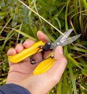 A gardener cuts a plant stalk with a pair of ergonomic garden snips