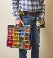 A man carries a drill and an Allit Pro 23-compartment case, with bins of screws visible inside