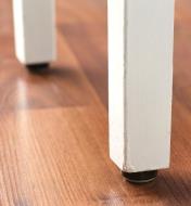 A chocolate color furniture slider attached to a furniture leg makes contact with the floor
