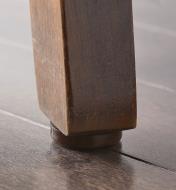 A chocolate color furniture gripper attached to a furniture leg makes contact with the floor