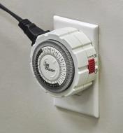 A close view of the mechanical timer connected to the grow-light cord and plugged into a wall outlet