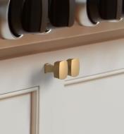 Two champagne bronze Stature square knobs mounted to two cupboard doors
