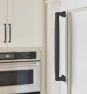 A matte black colored Stature handle is connected vertically to a white cupboard door