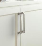 Two satin nickel colored Stature handles are connected vertically to two white colored cupboard doors