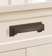An oil-rubbed bronze Appoint cup pull connected horizontally to a white drawer