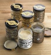 Six produits de finition Odie's avec étiquettes en français, dont deux pots ouverts, déposés sur une surface de bois