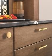 One champagne bronze knob and two champagne bronze handles attached to a cupboard and drawers