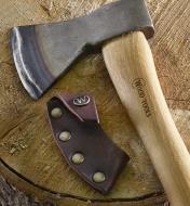 The leather sheath and carving axe rest on the end of a log