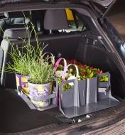 Cloisons pour coffre d'auto retenant de petits pots de fleurs et deux grands contenants des plantes solidement attachés à l'aide d'une sangle