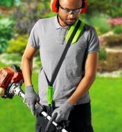 A man wearing the trimmer shoulder strap while using a grass trimmer