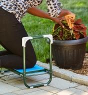 Personne agenouillée sur un agenouilloir-tabouret pliant prenant soin d’une plante en pot placée dans un jardin