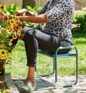 A woman sits on the folding kneeler stool while tending to an outdoor potted plant