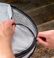 A gardener unzips the mesh top to remove it from the pop-up plant cover