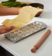 Laying a sheet of rolled-out pasta dough on top of the ravioli mold
