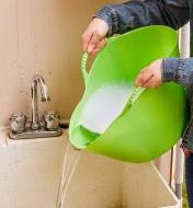 Personne tenant les poignées d’un panier de jardin de 14 L en le pliant légèrement pour déverser l’eau savonneuse dans un évier 