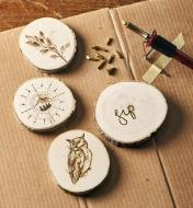 Four aspen rounds adorned with wood-burned designs next to the heat pen and interchangeable nibs