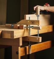 A person planes a workpiece that is held on a workbench with a wooden handscrew