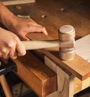 A cabinetmaker’s mallet being struck against a plank of wood