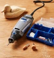 A rotary tool sits on a wood surface between an accessory kit and a wooden duck