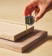 Personne mesurant l’épaisseur d’une planche de bois avec un ruban à mesurer porte-clés