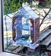 A window bird feeder mounted on the outside of a window, seen from inside the house