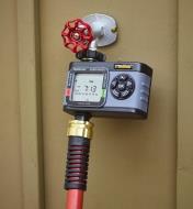 A garden hose connected to a one-zone electronic water timer mounted on an outdoor faucet