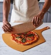 A cook uses an Epicurean pizza rocker to slice a homemade pizza on an Epicurean pizza peel