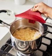 Personne attachant une passoire à pince rouge à une casserole contenant des pâtes et de l'eau