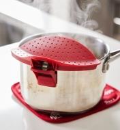A red Clip and Drain attached to a pot, sitting on a white countertop