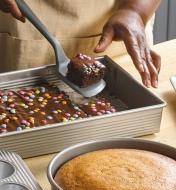 Using a spatula to remove chocolate cake slices from the rectangular baking pan