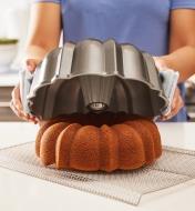 A cake being removed from a Bundt pan onto a cooling rack