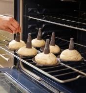 Six bagels on conical molds are being placed into an oven