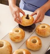 Five cooked bagels are on a cooling rack while one bagel is removed from a mold